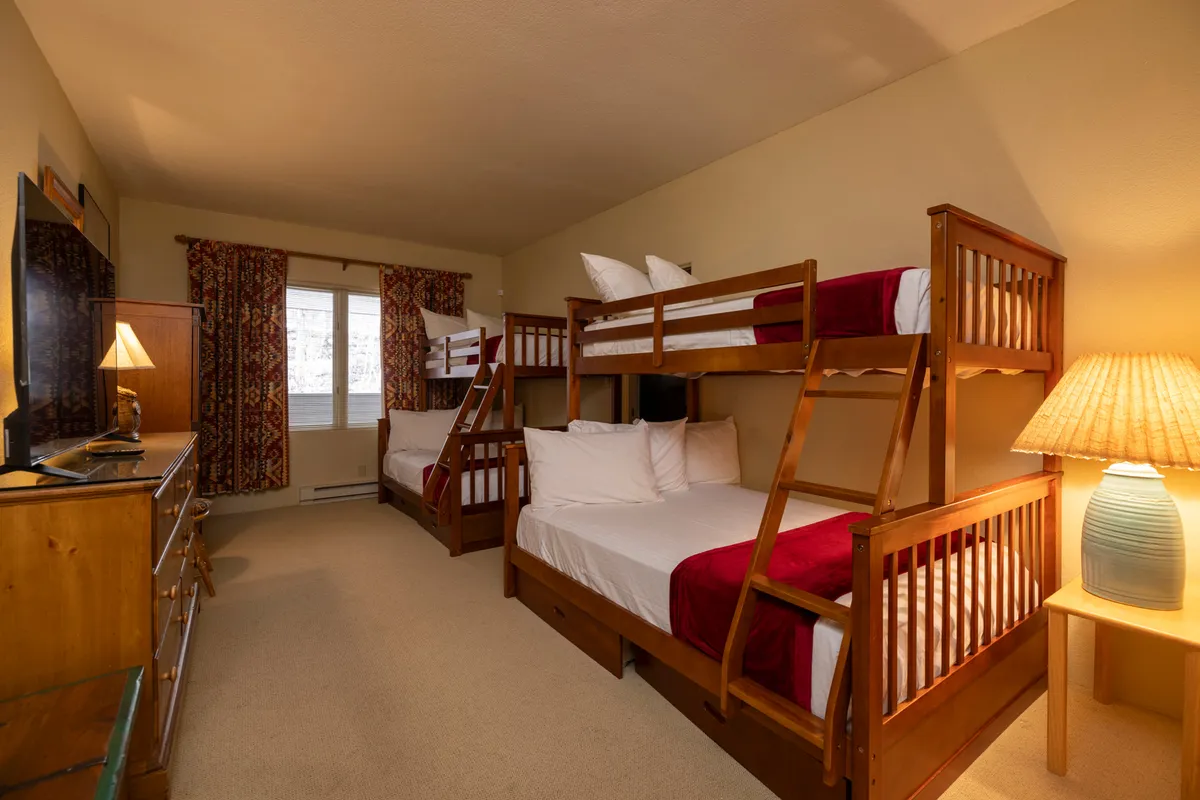 A comfortable bedroom featuring bunk beds, a dresser, and a lamp, complemented by curtains that create a cozy, family-friendly environment. Perfect for kids or teens to unwind and share stories.
