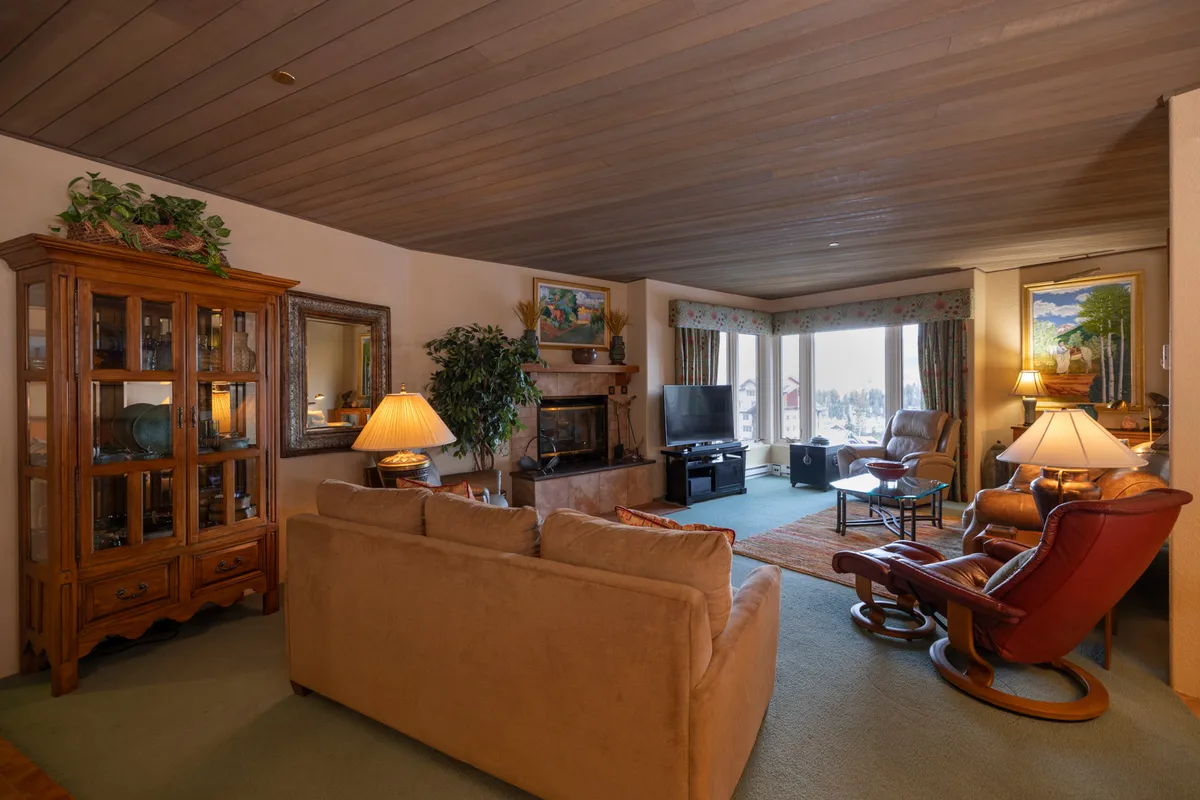 A comfortable living room with a sofa and recliner positioned around a roaring fireplace, large windows letting in natural light, and an entertainment center for movie nights. The scene is warm and welcoming, ideal for evenings spent indoors with friends or family.
