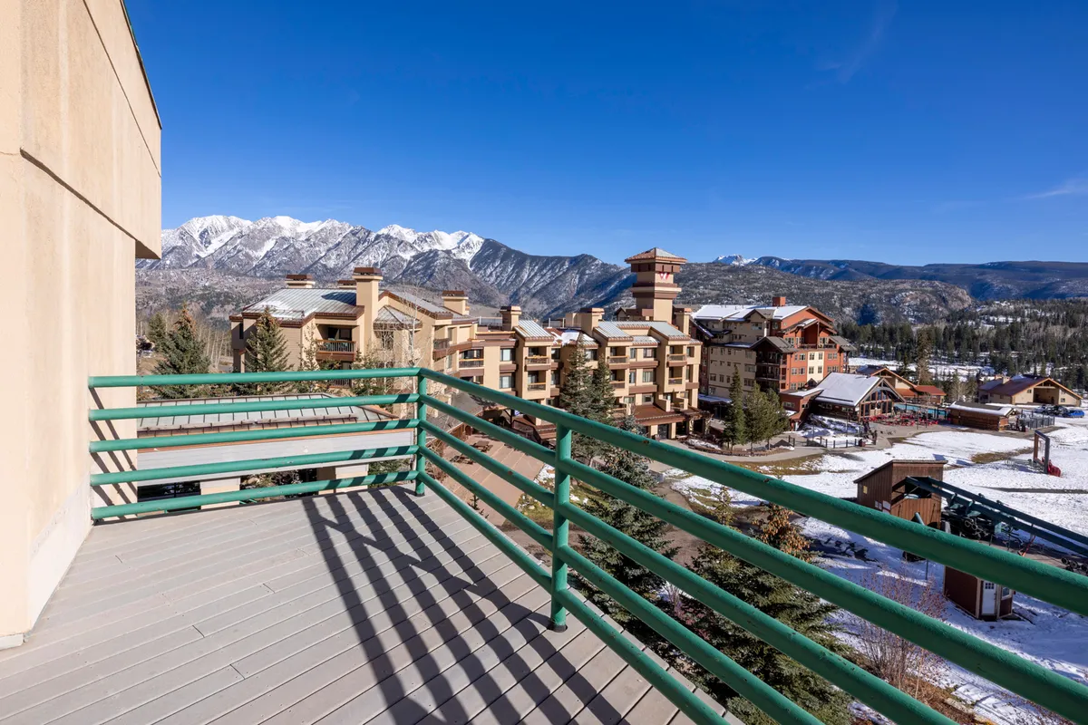 A tranquil mountain range view from a balcony, with the resort buildings and a balcony railing in the foreground. The setting evokes the peacefulness of mountain evenings and opportunities for family gatherings outdoors.
