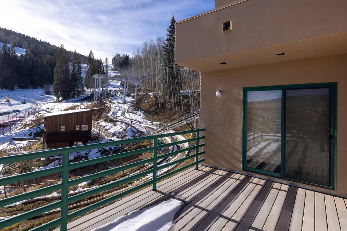 A snow-covered landscape with a ski lift in the background, viewed from a balcony with a railing. The forest backdrop and visible ski activity create a lively, adventurous winter atmosphere right outside the door.
